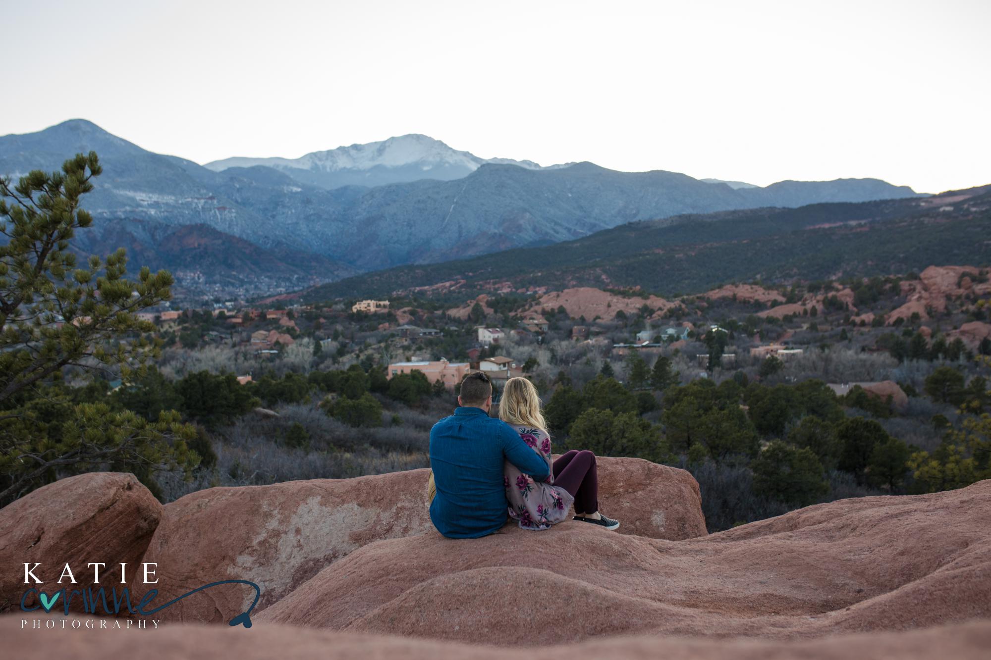 surprise proposal couple sits in Garden of the Gods overlooking mountains