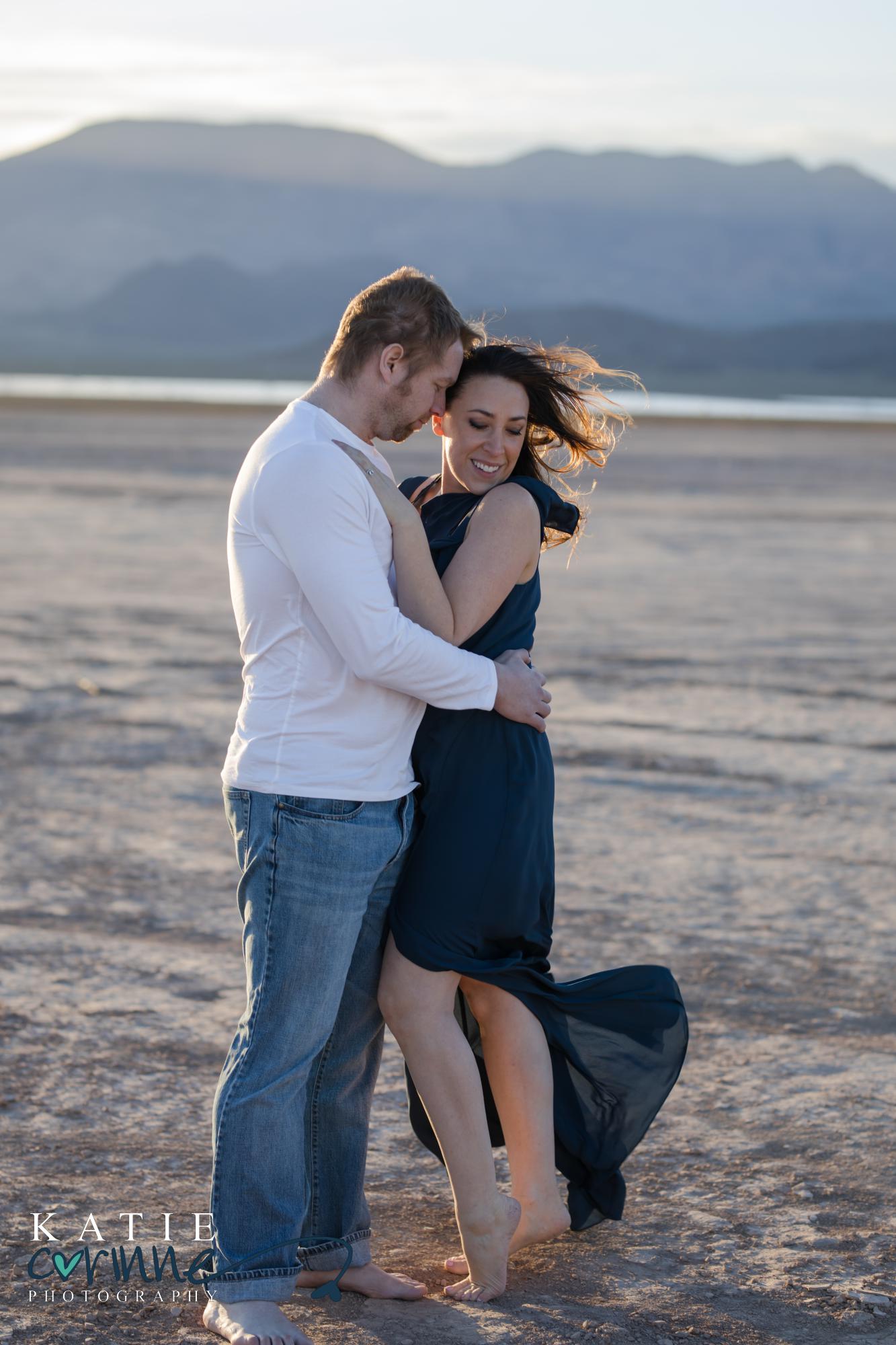 windswept couple hold each other in front of mountain range