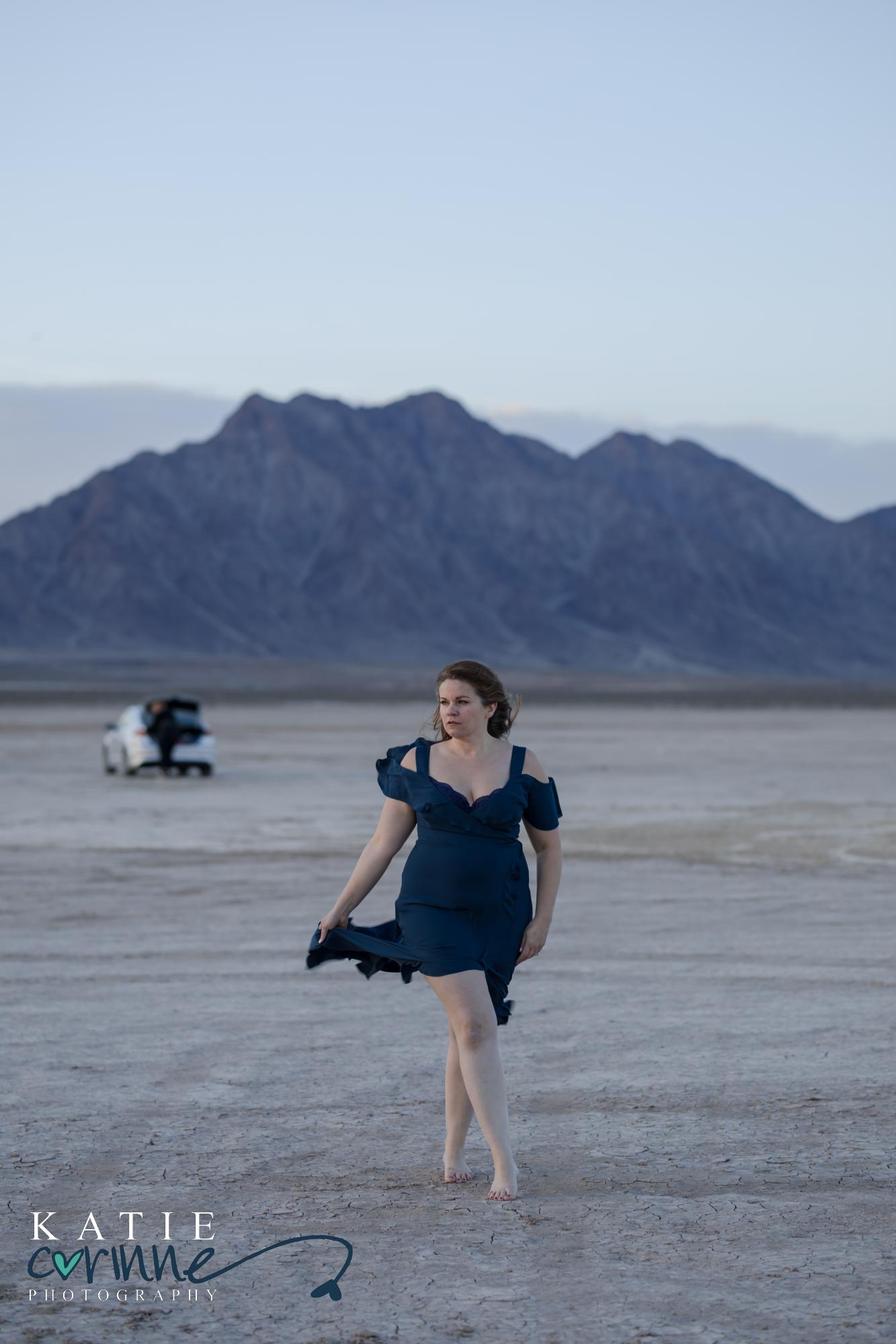 woman holds train of dress and walks across dry lake bed