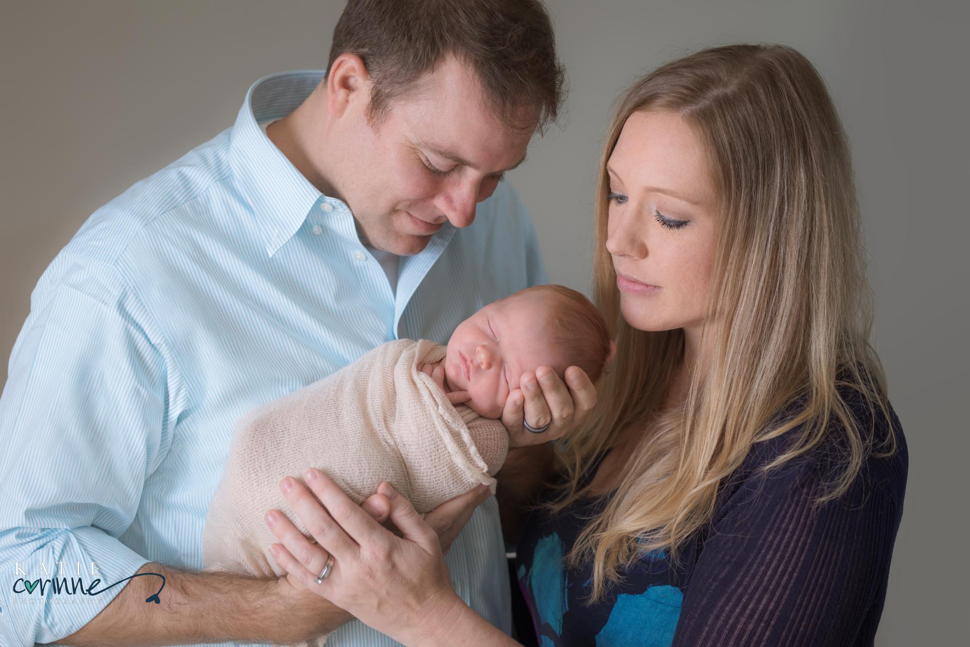 Parents hold new baby girl against plain backdrop