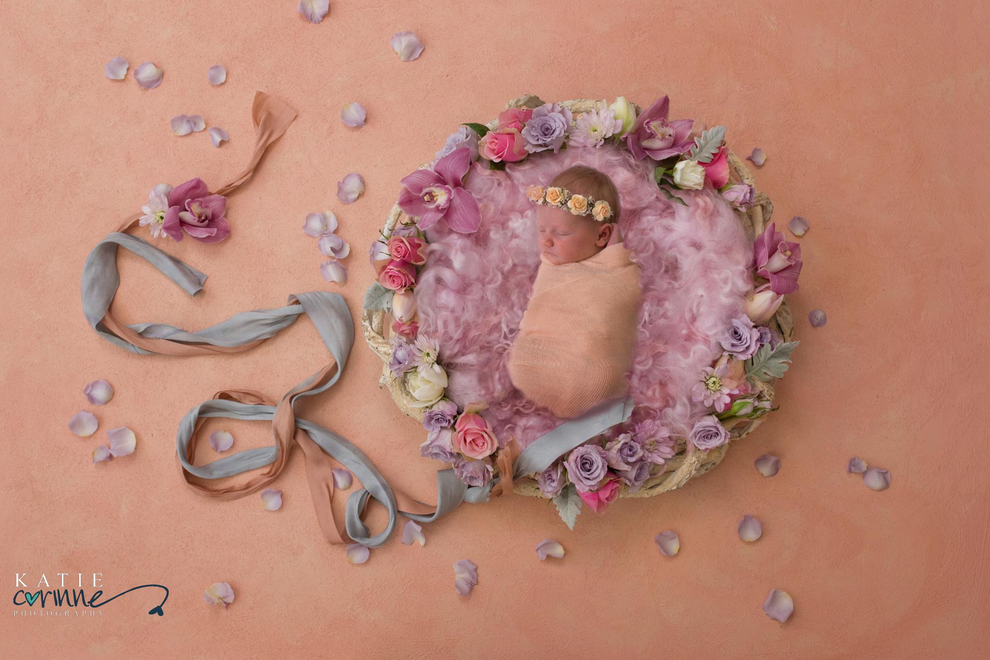 Newborn baby girl posed among flowers and ribbons