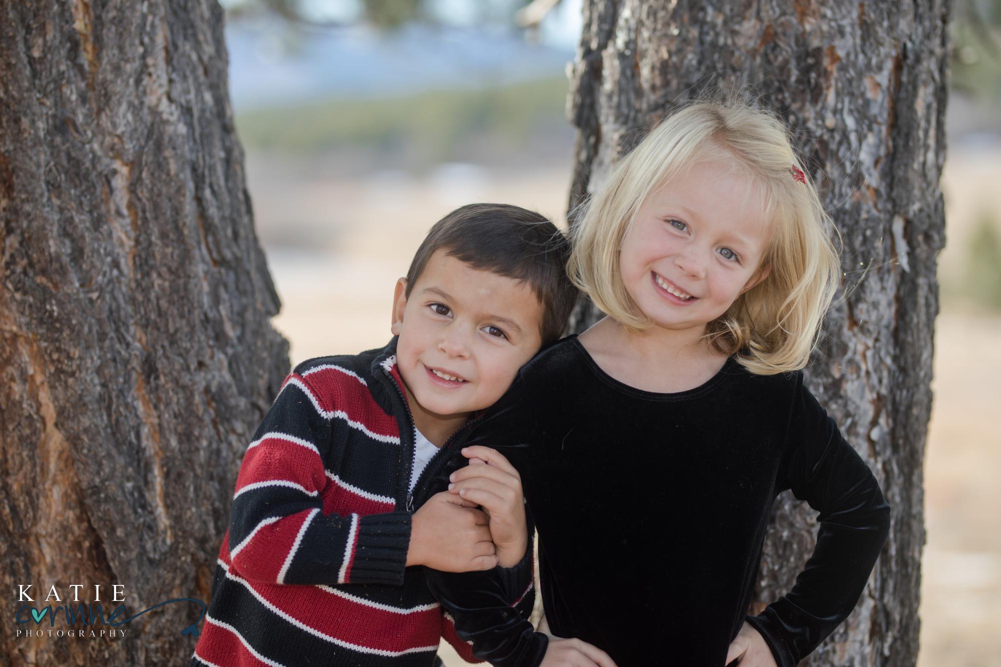 younger brother holds older sister while smiling at camera