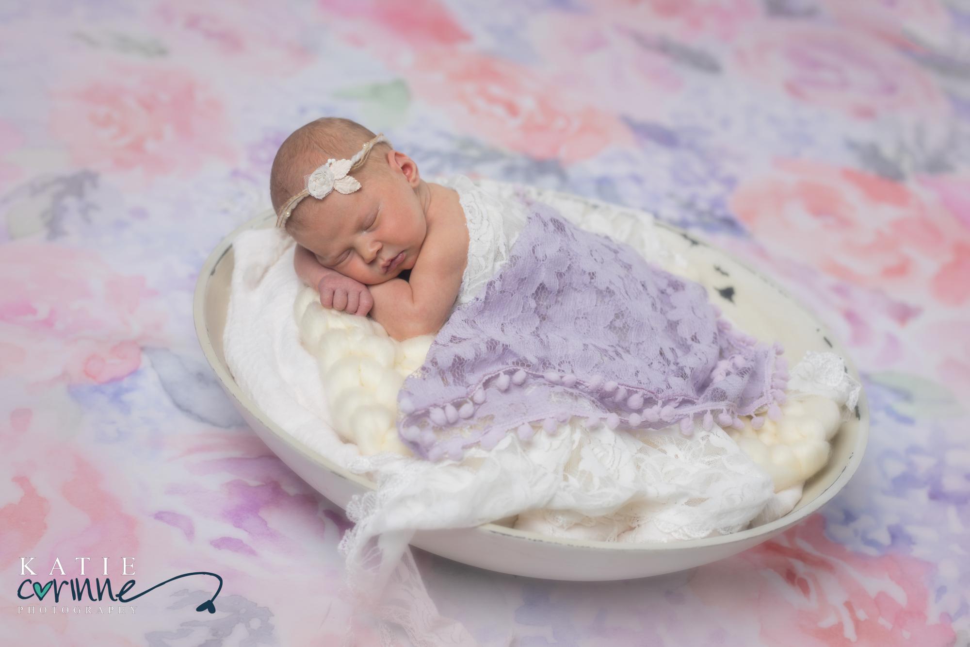 newborn baby girl photographed against backdrop of watercolor painted flowers