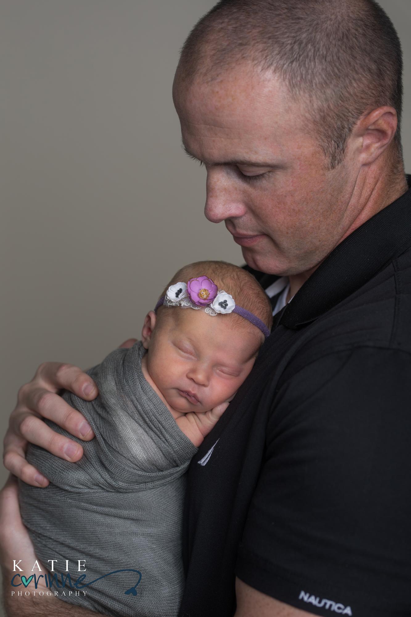 girl baby rests against father's chest wearing purple headband