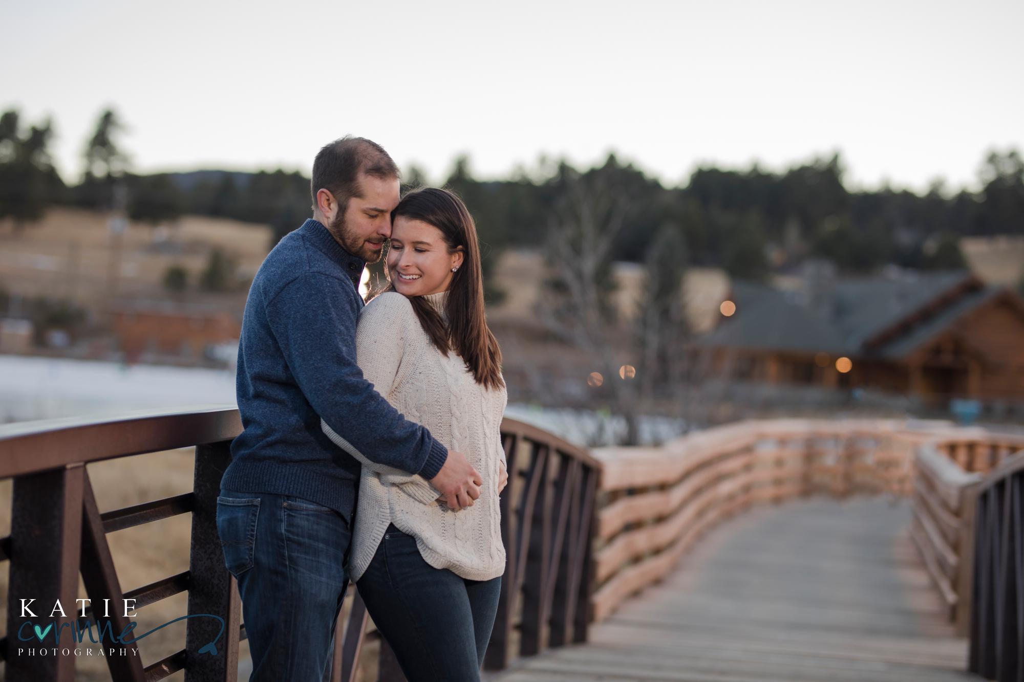 couple pose on bridge in front of Evergreen lake house