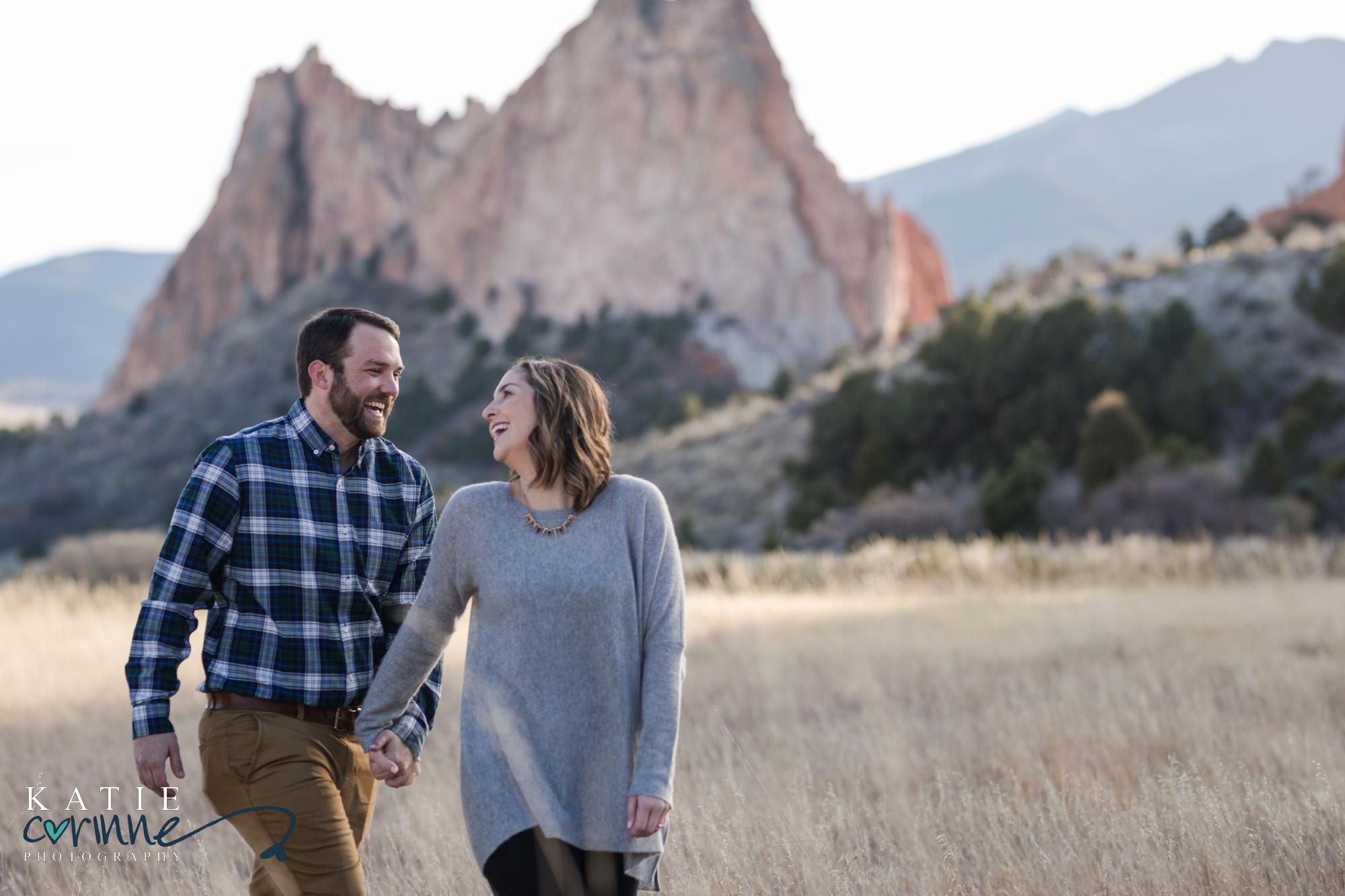 colorado springs couple laugh and hold hands in front of red rocks