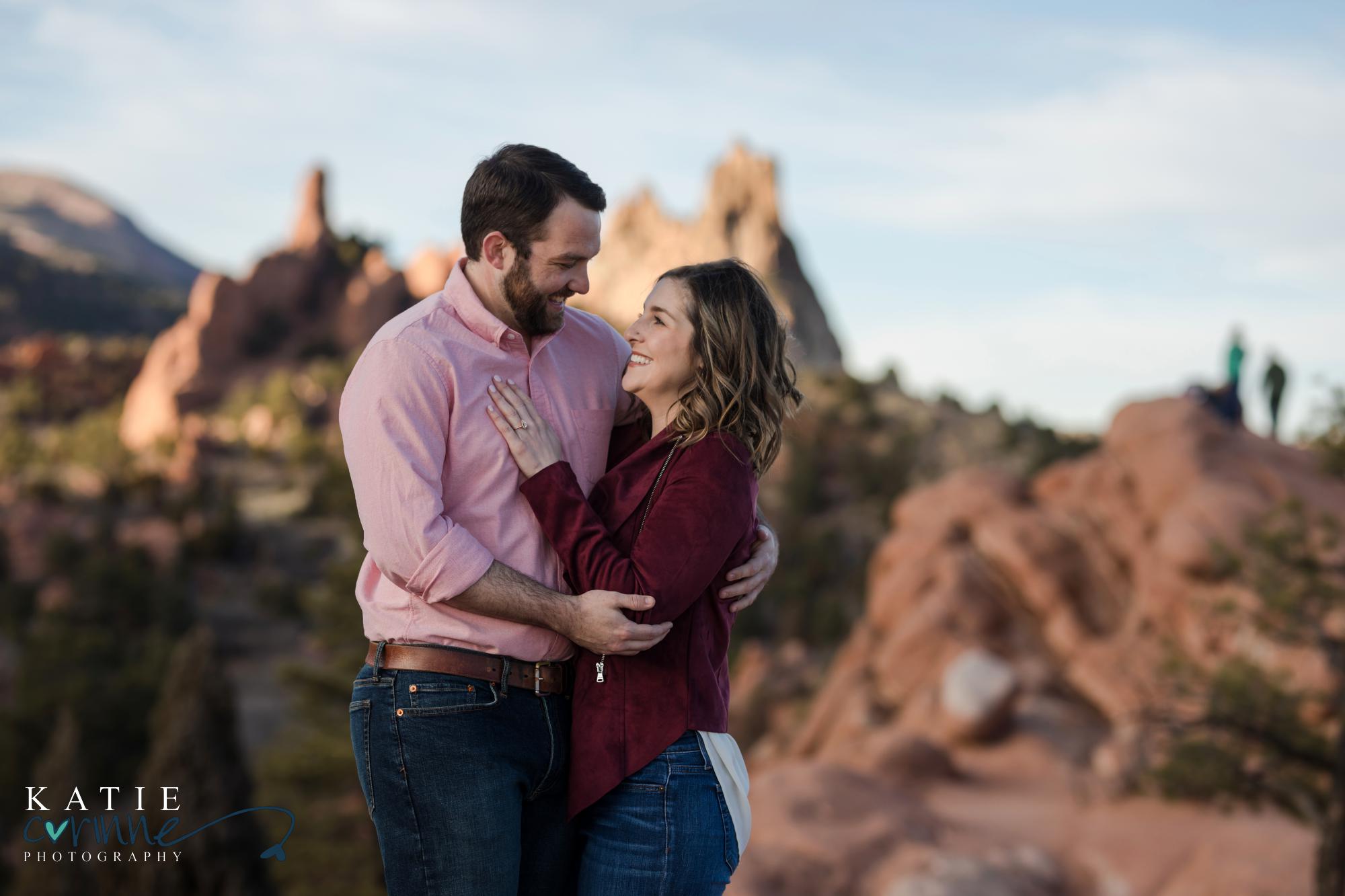 engaged couple looks at each other smiling in front of garden of the gods