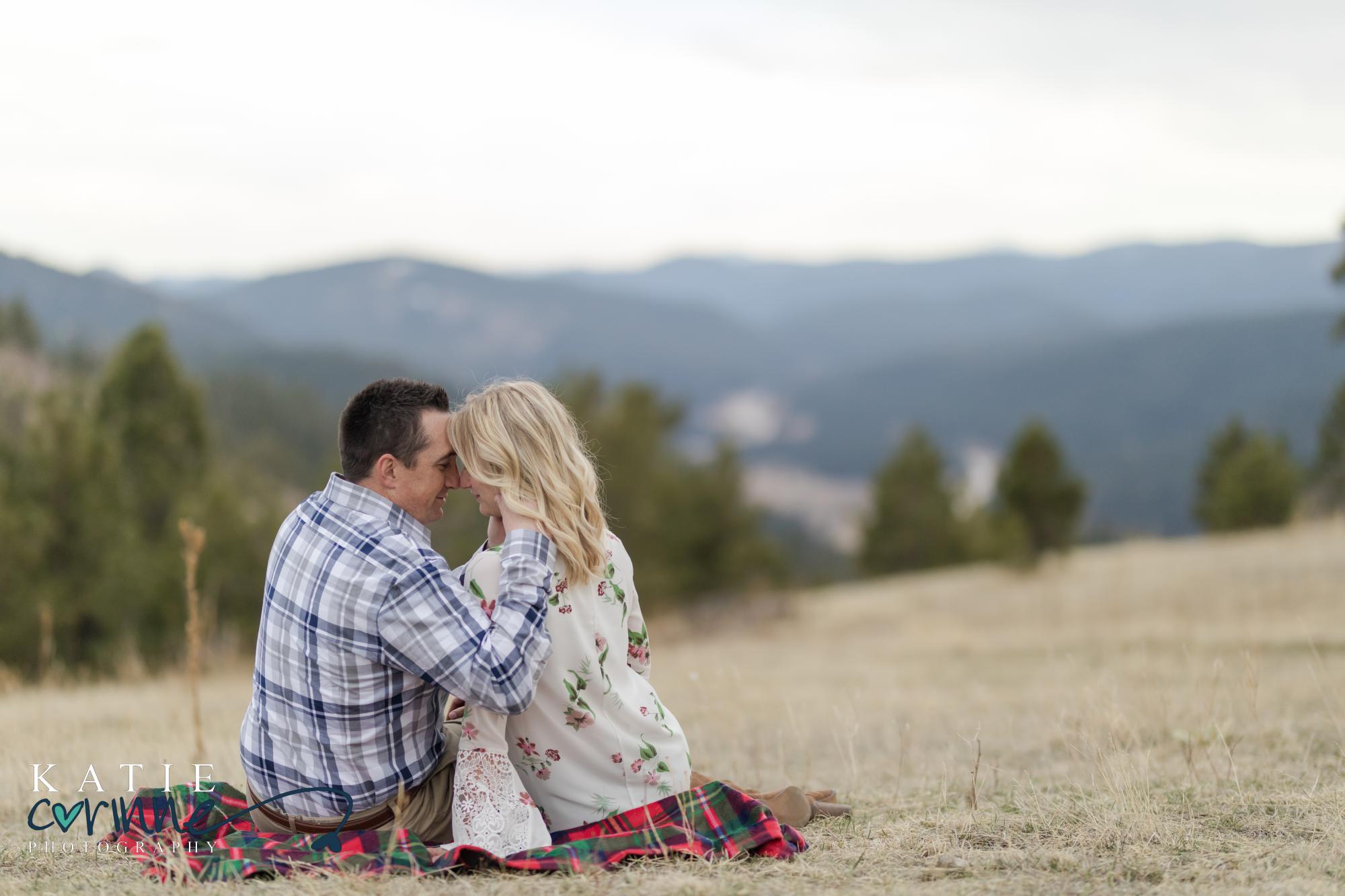 Colorado engaged couple sits on blanket overlooking mountains