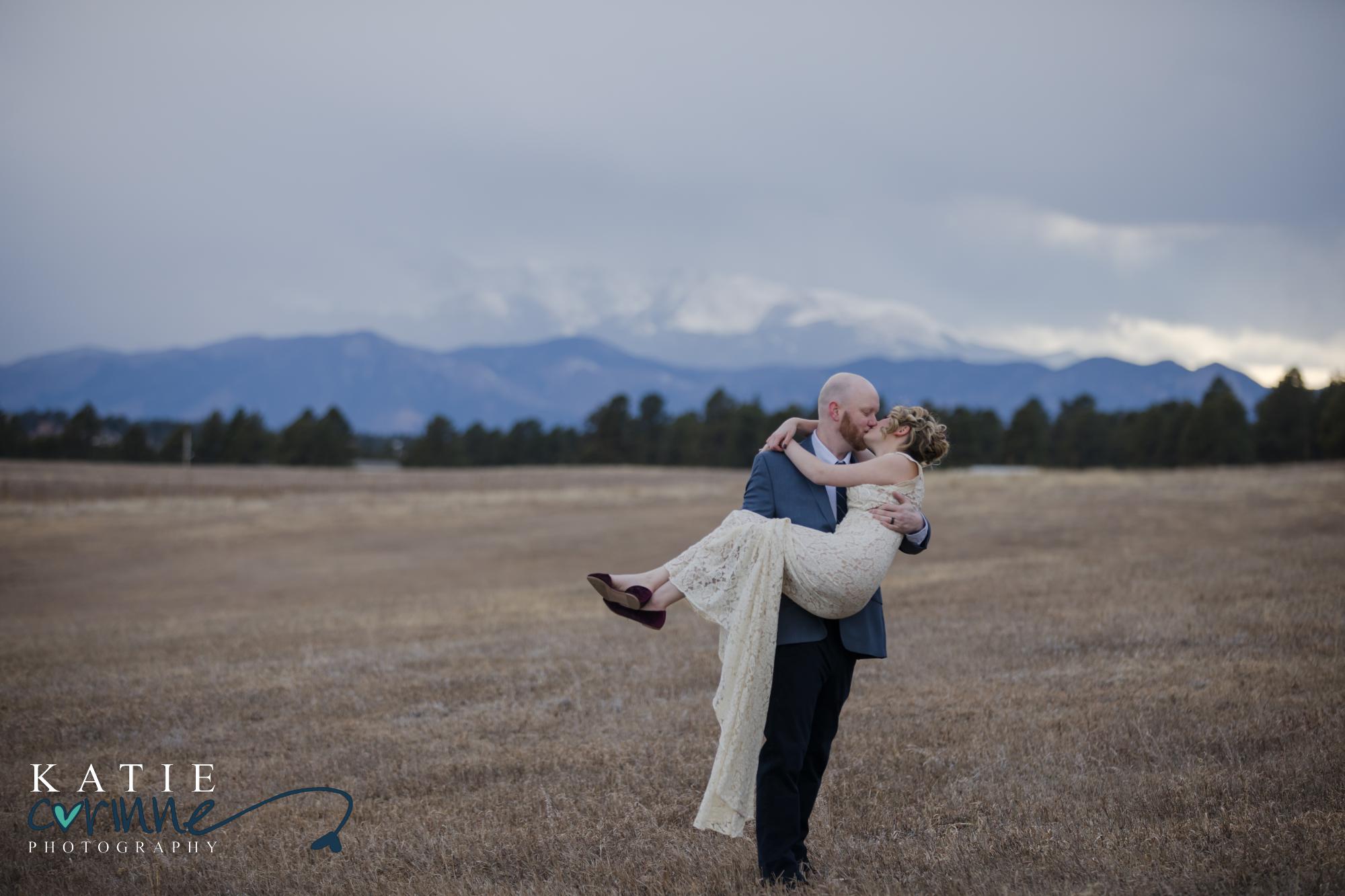 Bride carries groom and couple kisses in front of mountains