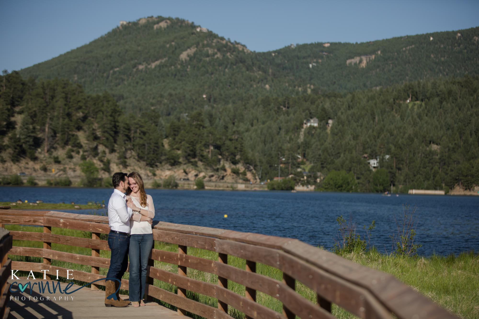 engaged couple on bridge over evergreen lake