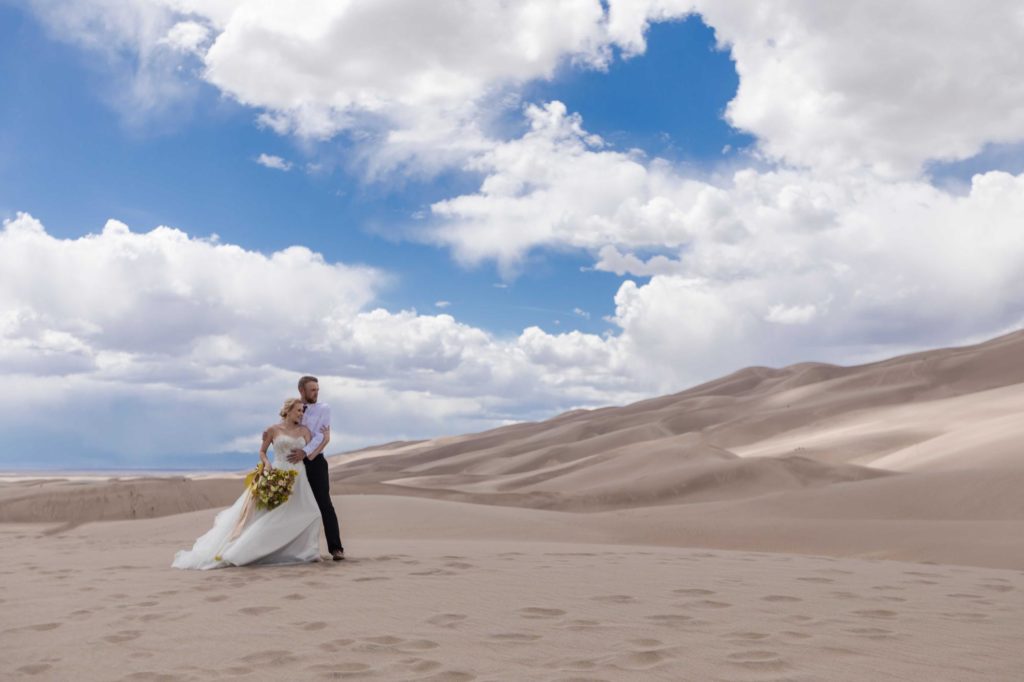 Wedding couple holds each other at sand dunes