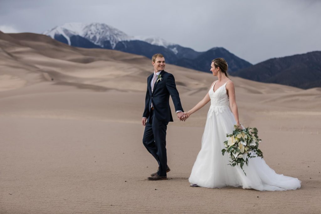 wedding couple hold hands on sand dunes