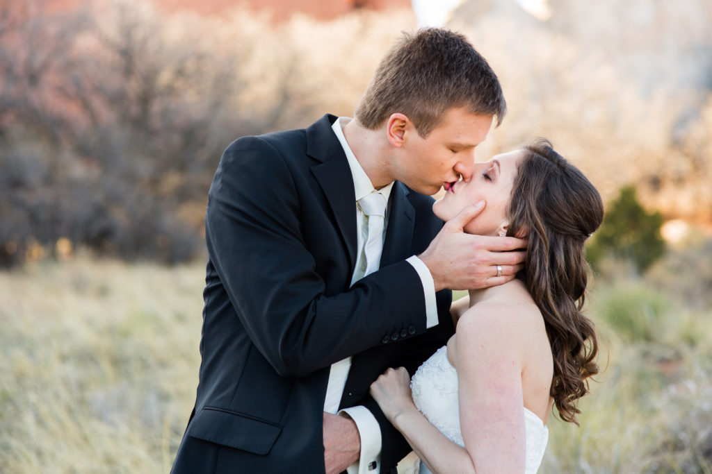 Eloping couple kiss in front of red rocks