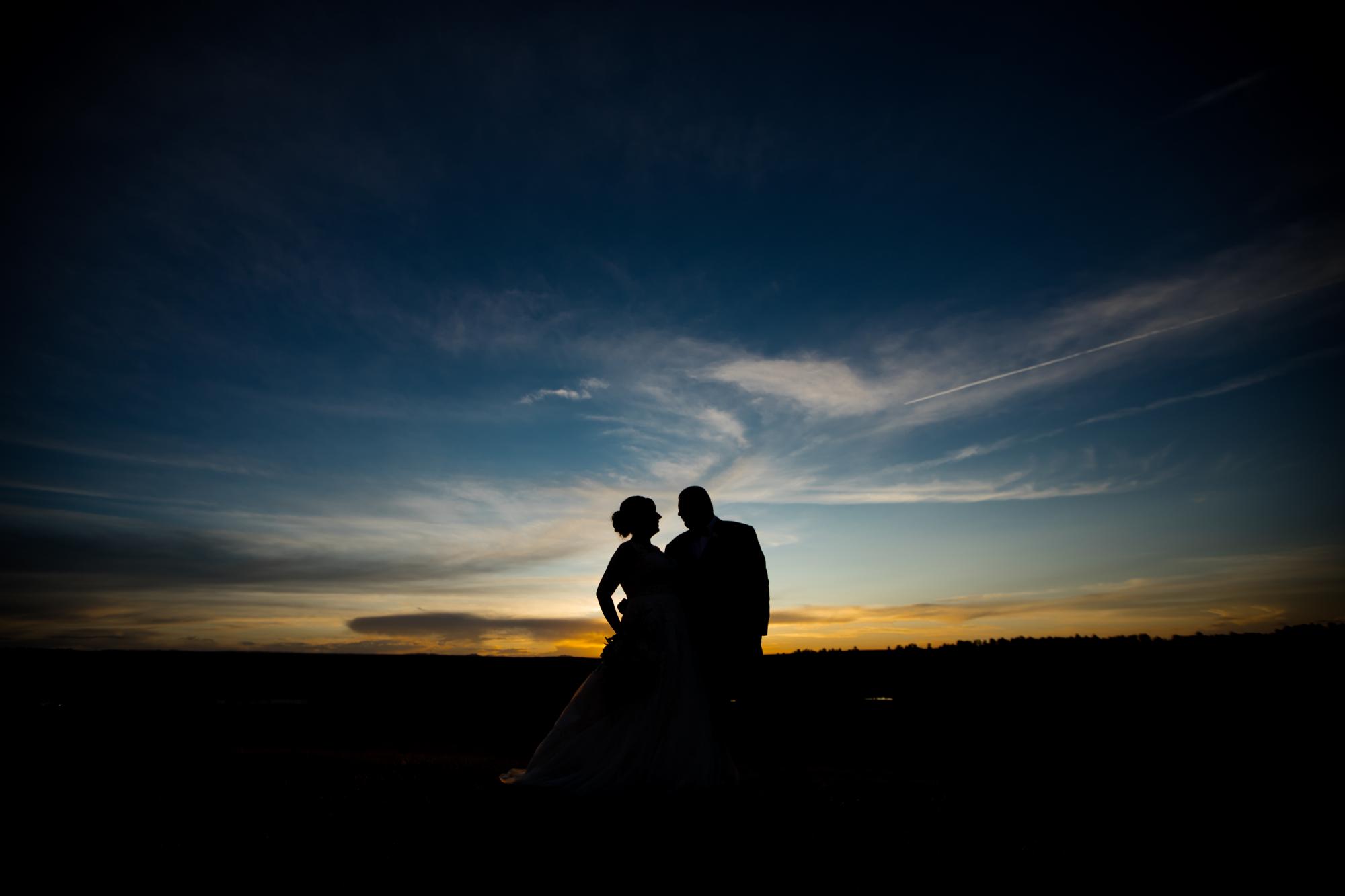 bride and groom are silhouetted against the sunset 