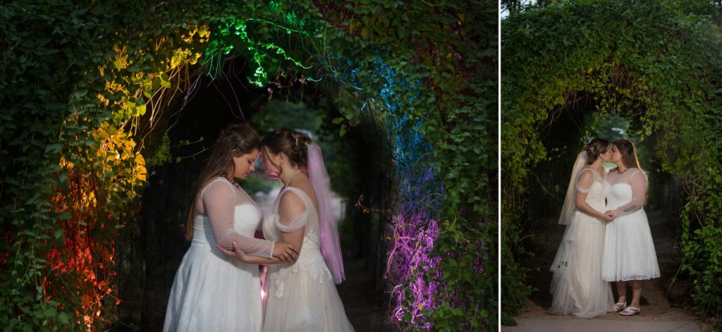 lesbian couple hold each other under rainbow arch