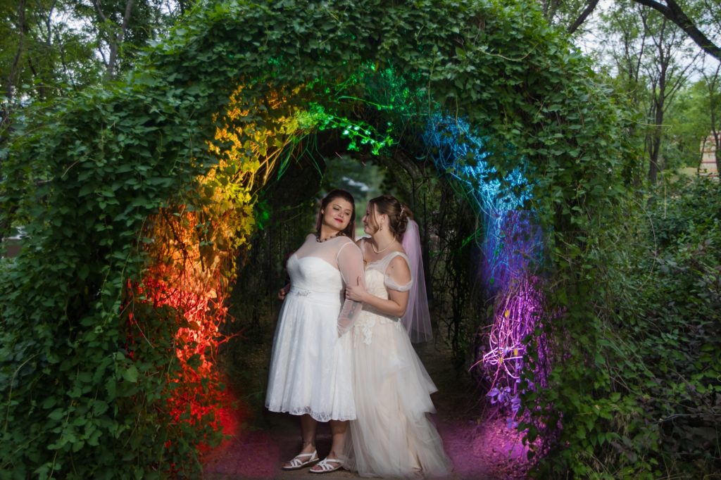 Newlyweds under rainbow arch at lgbt wedding