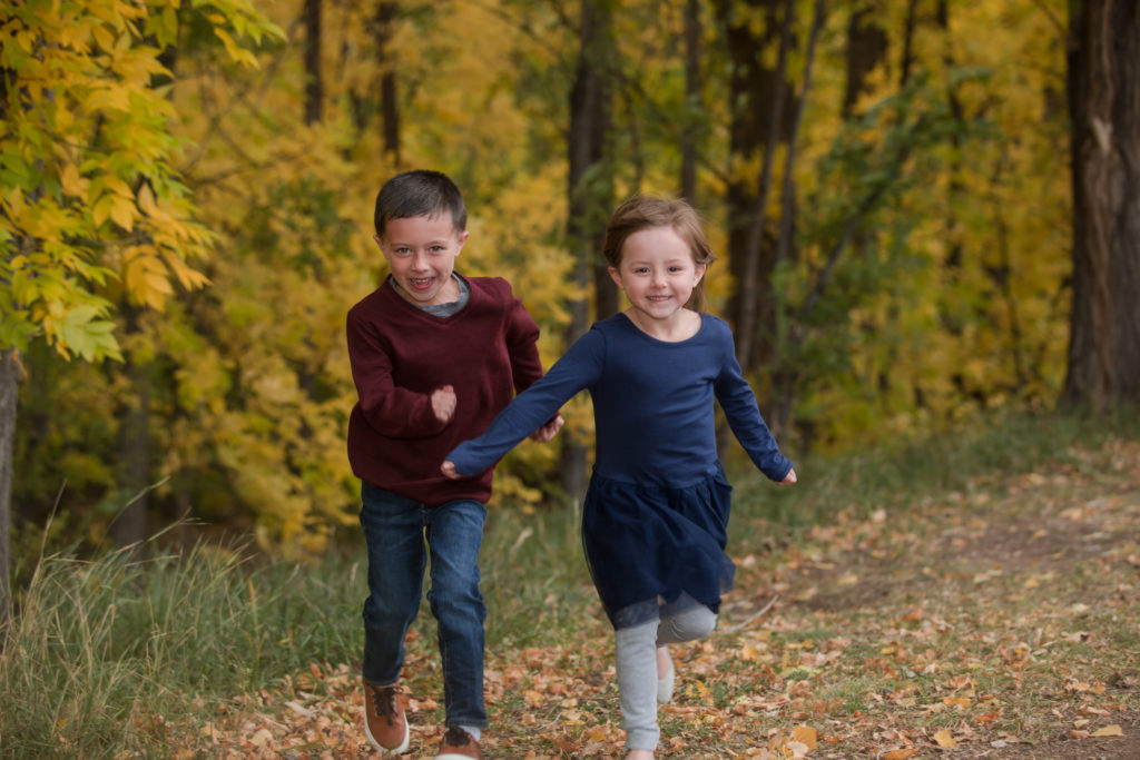 brother and sister running in fall leaves