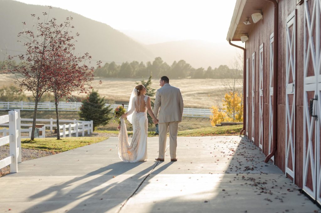 bride and groom walking along red barn