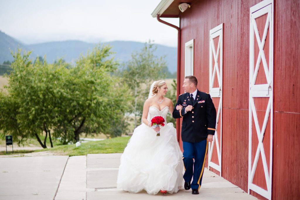 bride and military groom walking along red barn