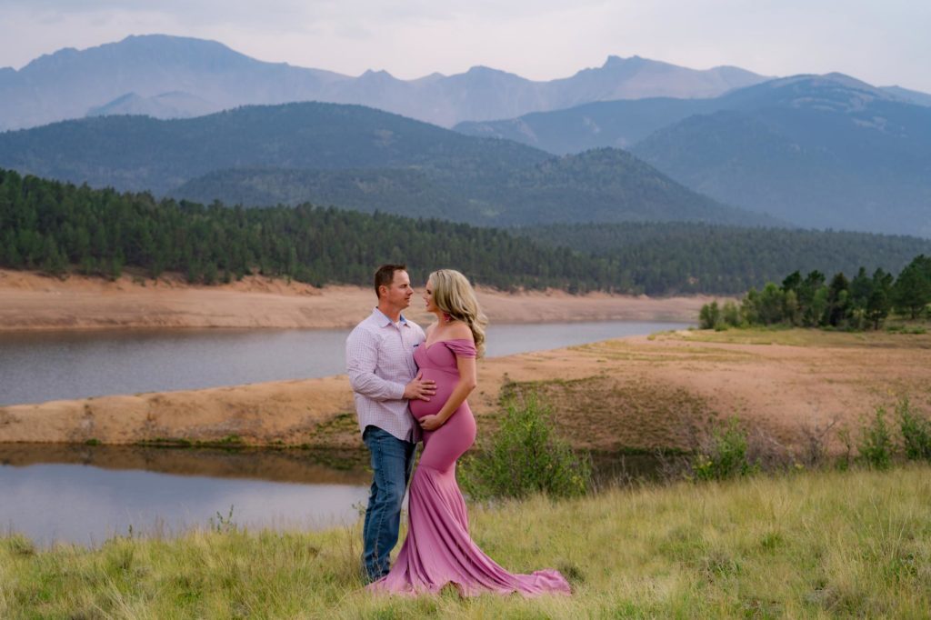 pregnant couple poses in front of rocky mountains