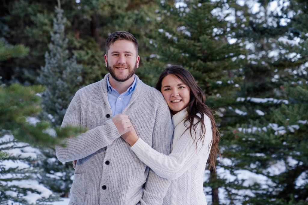 couple looks at camera in front of Colorado evergreens
