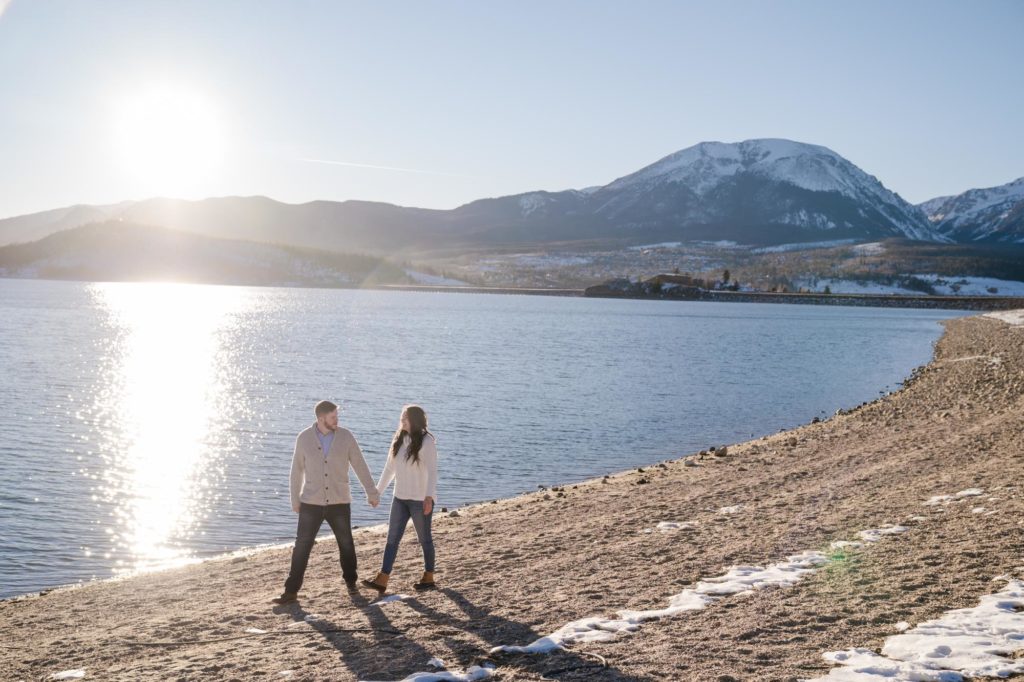 newly engaged couple walk along beach at Lake Dillon