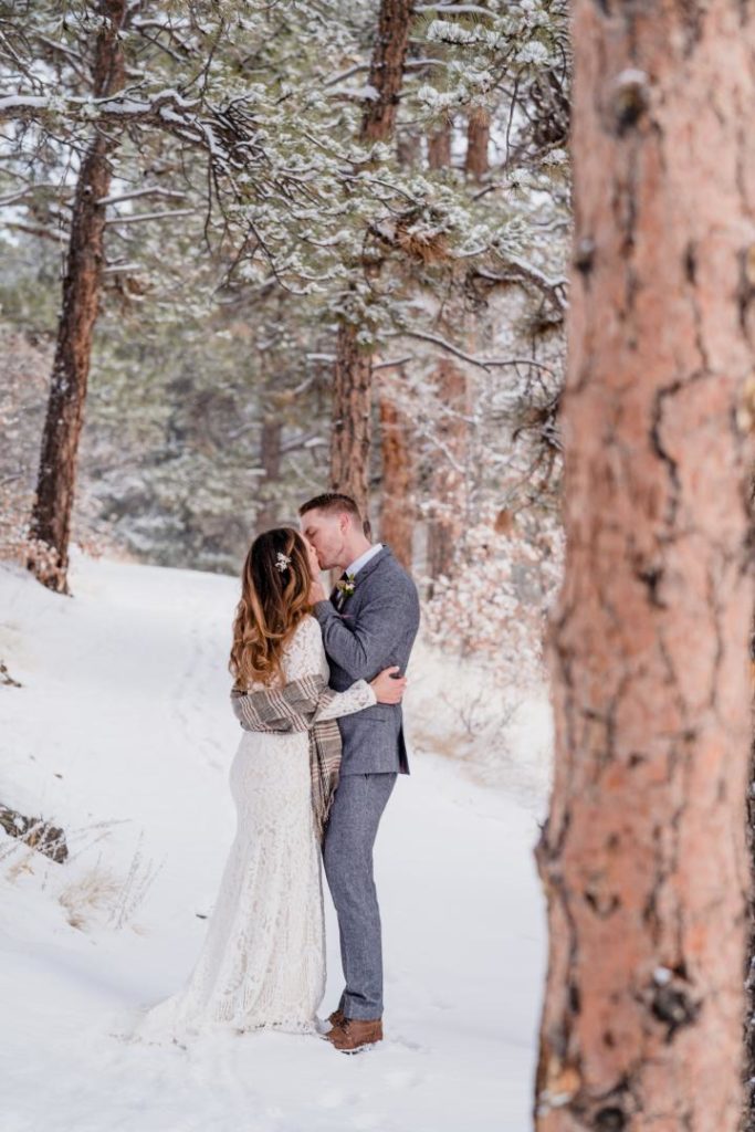 bride and groom kissing in snowy colorado forest