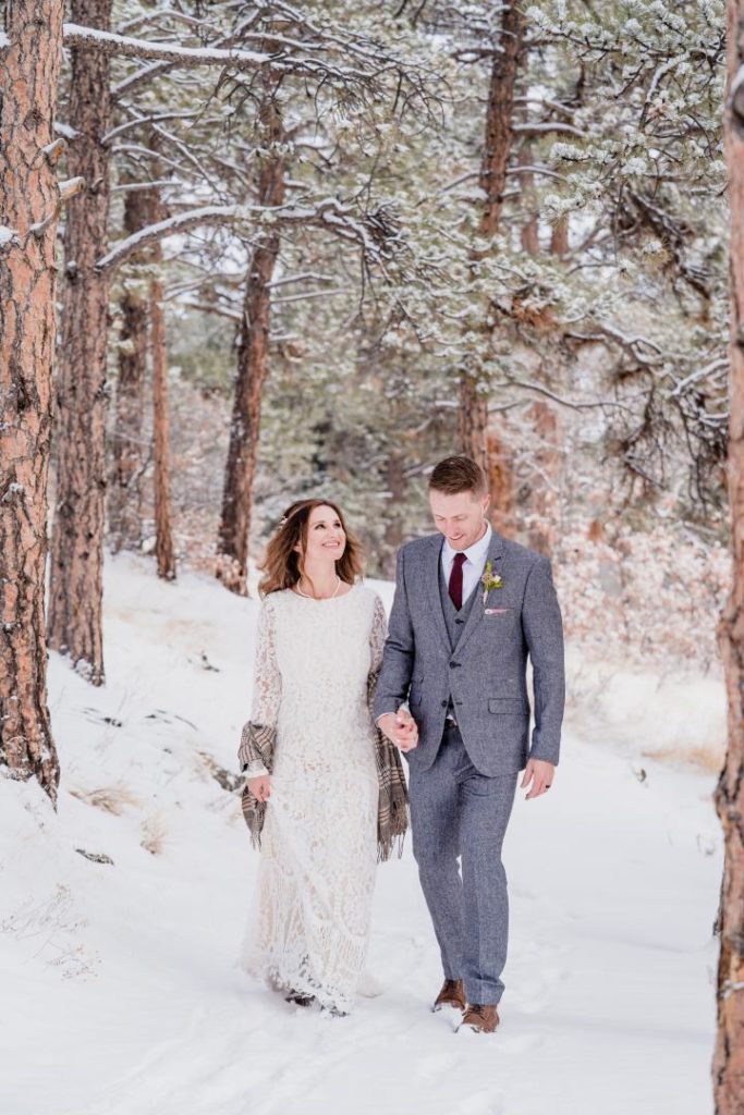 bride and groom walking through snowy colorado forest